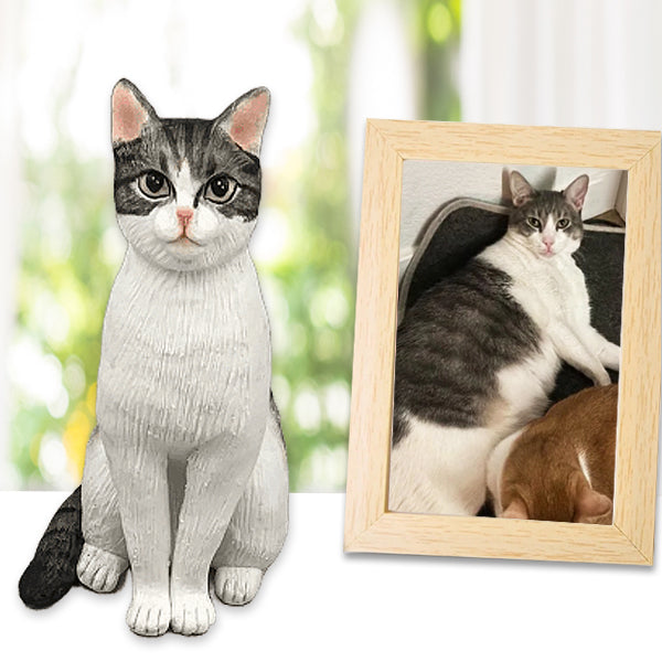 A gray and white cat wedding cake topper next to a framed photo of the same cat.